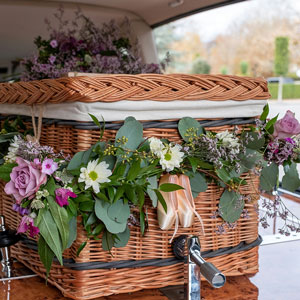 photograph of a wicker coffin covered in flowers