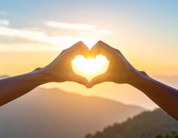 a photo of two hands making a heart shape in front of the evening sun