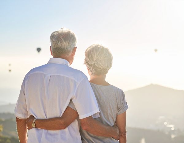 a photo of an elderly couple looking out towards a field with hot air balloons in the sky